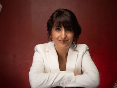 Kully Bath in white blazer with floating books, smiling confidently against a deep red background.