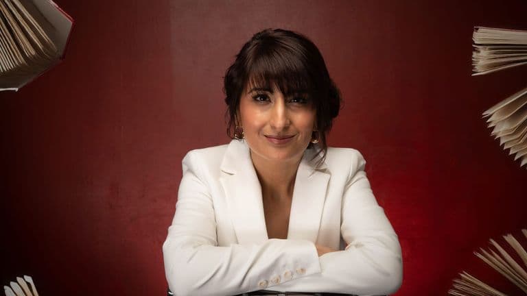 Kully Bath in white blazer with floating books, smiling confidently against a deep red background.