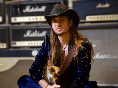 Ulrich Ellison, founder of Total Guitar Transformation (TGT), sitting with a guitar in front of Marshall amplifiers, embodying his passion for music and teaching. TGT's innovative, personalized approach helps adult learners over 40 rediscover their love for guitar through practical, creative methods inspired by legendary musicians like Jimi Hendrix