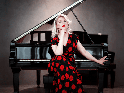 Ellen Fischerová in a black-and-red floral dress seated beside a grand piano.