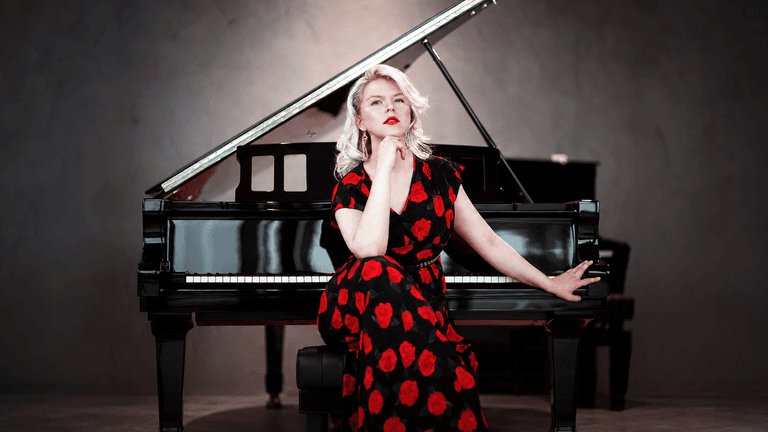 Ellen Fischerová in a black-and-red floral dress seated beside a grand piano.