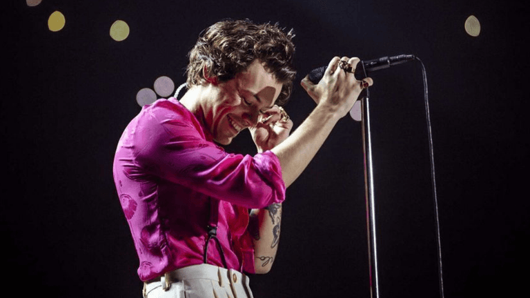 A singer in a pink shirt performs on stage, smiling and holding a microphone