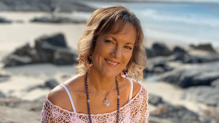Smiling woman in a pink crochet top by the beach with rocks in background