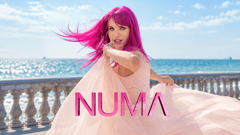 A woman with pink hair dances gracefully by the sea, wearing a flowing dress