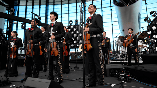 A mariachi band performs on stage with instruments and traditional attire in a modern venue