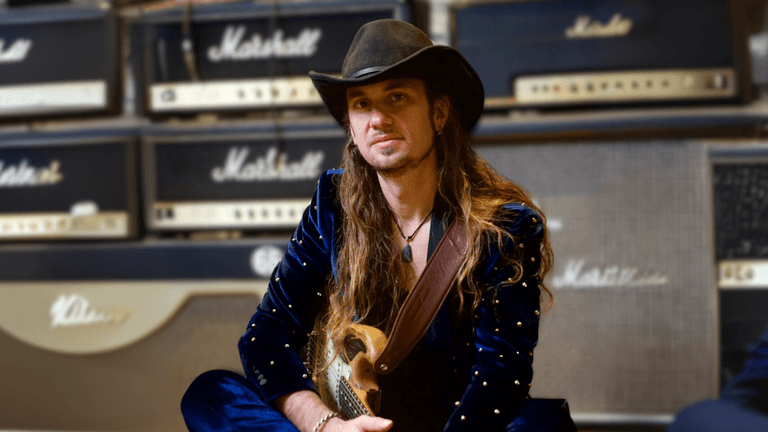 Ulrich Ellison, founder of Total Guitar Transformation (TGT), sitting with a guitar in front of Marshall amplifiers, embodying his passion for music and teaching. TGT's innovative, personalized approach helps adult learners over 40 rediscover their love for guitar through practical, creative methods inspired by legendary musicians like Jimi Hendrix