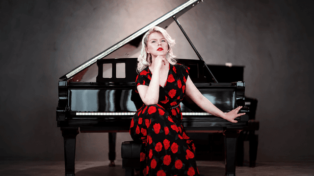 Ellen Fischerová in a black-and-red floral dress seated beside a grand piano.