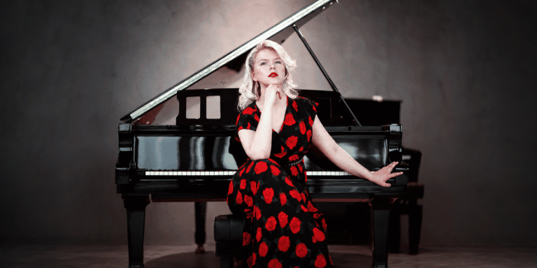 Ellen Fischerová in a black-and-red floral dress seated beside a grand piano.